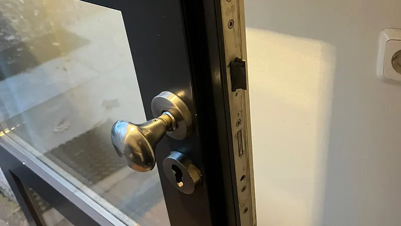 Hang- en sluitwerk vervangen in Eindhoven — RVS deurknop en cilinderrozet op een zwarte stalen deur met glas, voorplaat van het slot in de deurkant